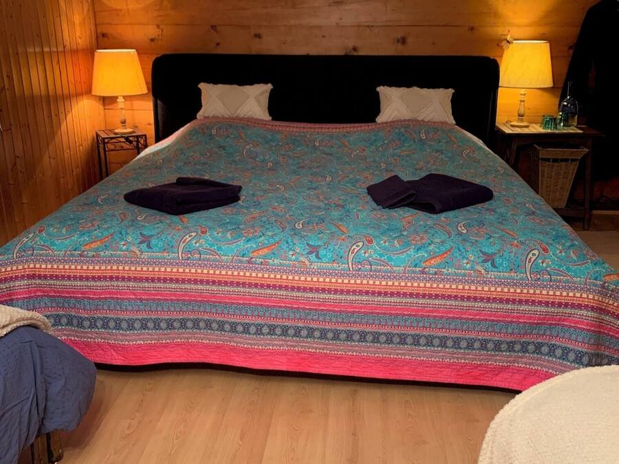 A wooden-paneled room with a bed, two bedside lamps, and a wicker chair.