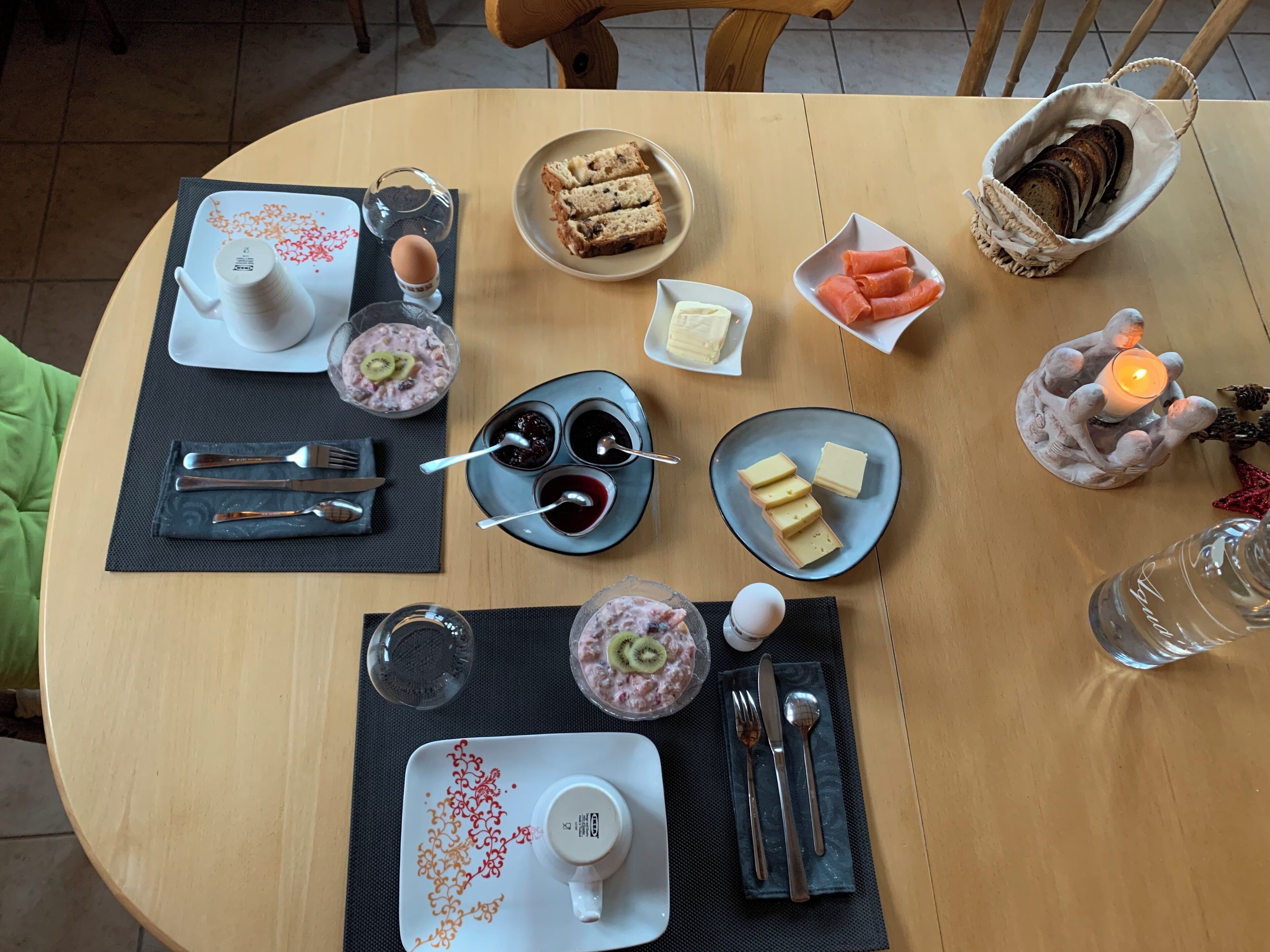 Une table à manger dressée avec différents plats, couverts et une bougie.