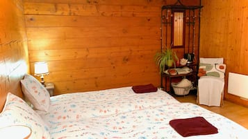 Ein Zimmer aus Holz mit einem Bett, einem Nachttisch, einer Lampe, einem Spiegel, einem Stuhl und einem kleinen Tisch mit einer Pflanze.