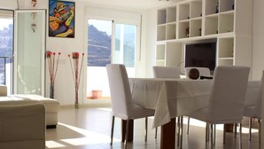 A modern dining area with a white table set for six, surrounded by white chairs. A television is mounted on the wall, and there are shelves above the table. - Stunning Central Penthouse with Breathtaking Sea and Mountain Views (Benalmádena)