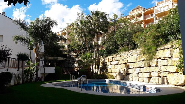 A swimming pool surrounded by greenery and stone walls, with a building in the background. - Stunning Central Penthouse with Breathtaking Sea and Mountain Views (Benalmádena)