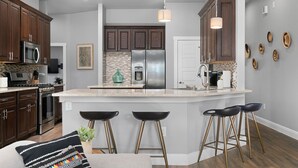 Une cuisine moderne avec des meubles de couleur bois foncé, des appareils en acier inoxydable et un îlot central doté de tabourets.