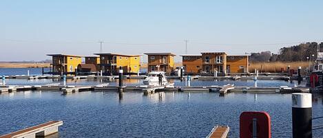 A marina with several docked boats, a wooden pier, and a row of yellow buildings with a flat roof.