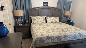 Un dormitorio con una cama grande, dos mesitas de noche, un tocador, un banco y un letrero en la pared.