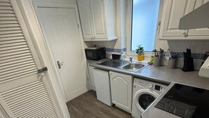 A compact kitchen with white cabinets, a built-in washing machine, a microwave, and a sink. - 1br-2guests-freeparking-wifi-tv (Wigston)