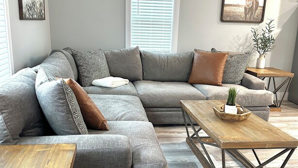 A modern living room with a grey sectional sofa, wooden coffee table, and a small side table with a plant. - Medina Square Retreat - Spacious 4 bdrm home walking distance to the square (Medina)