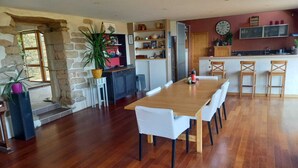 A spacious kitchen with a wooden dining table and chairs, a stone wall, and a large clock on the wall. - Spacious, comfortable farmhouse facing the sea (Locmaria-Plouzané)