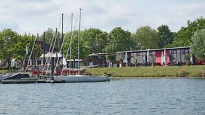 En småbåtshamn med flera segelbåtar förtöjda, en restaurang med uteservering och en byggnad med en röd fasad.