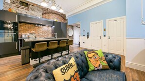 Eine moderne Küche mit Backsteinwand, einer Bar und einem Ledersofa mit einem Cartoon-Kissen.