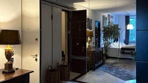 A modern interior with a marble floor, a wooden cabinet with a lamp, a mirror, and a bed with a plant. - Corvetto View (Genoa)