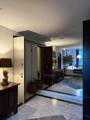 A modern interior with a marble floor, a wooden cabinet with a lamp, a mirror, and a bed with a plant.