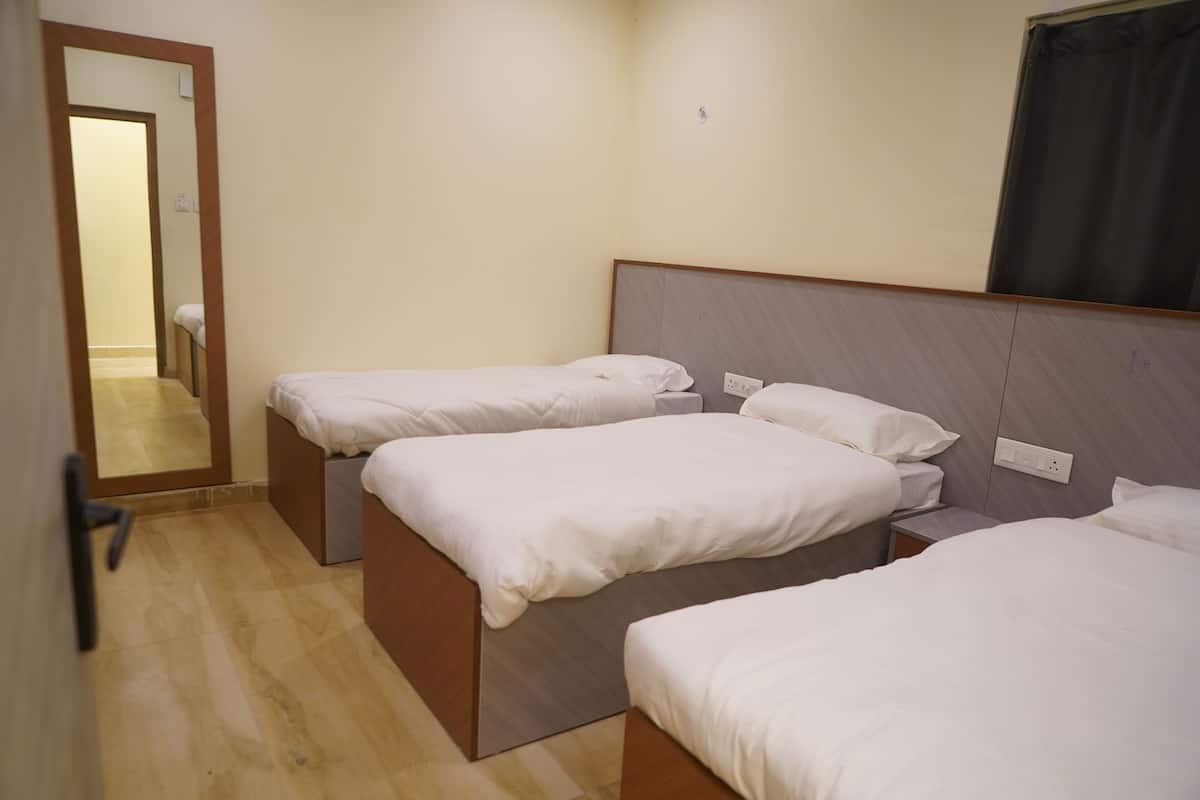 A hotel room with three single beds, a wooden floor, a mirror, and a window with a curtain.