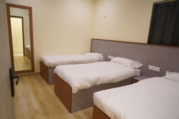 Una camera d'albergo con tre letti singoli, pavimento in legno, uno specchio e una finestra con tenda.