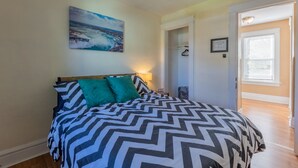 A bedroom with a bed, a nightstand, a wall clock, a door, and a hallway.