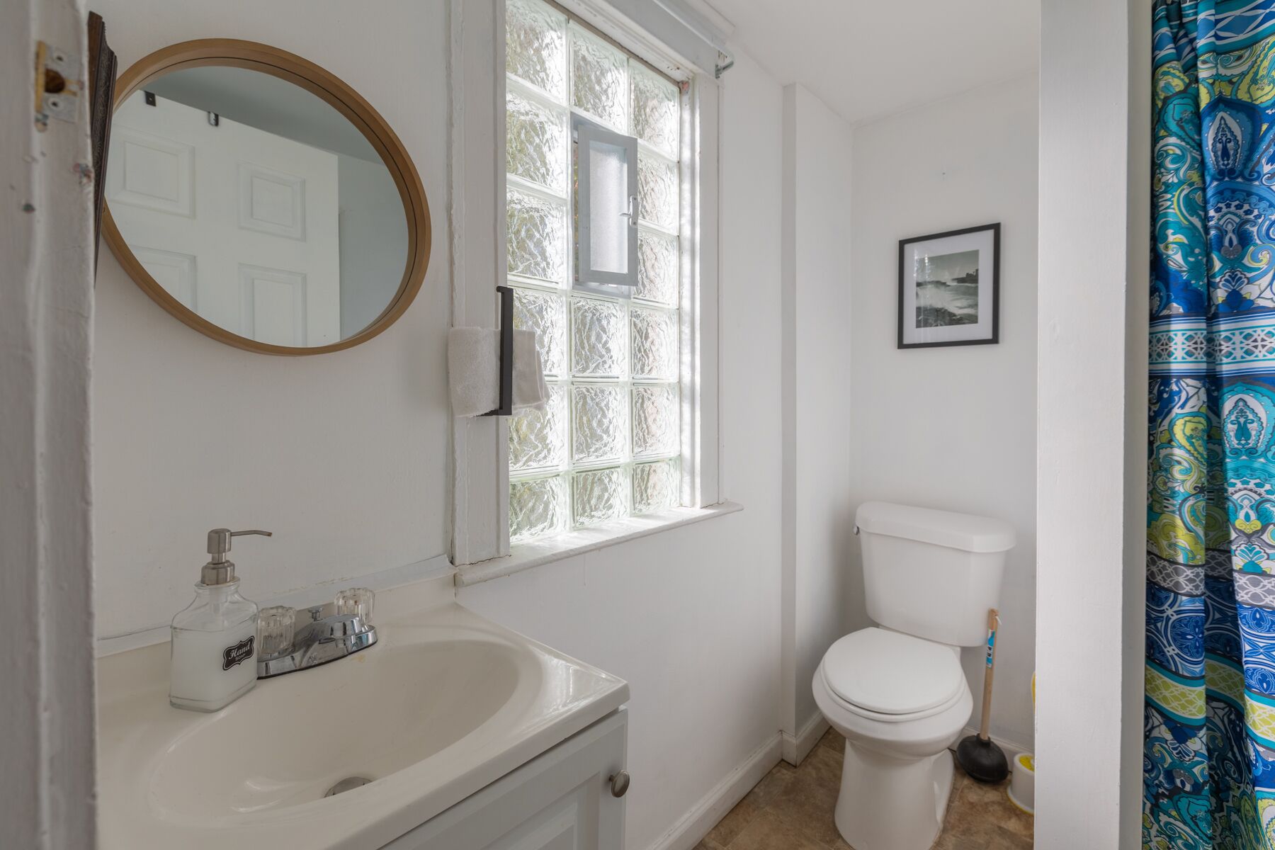 A bathroom with a white sink, a toilet, a window with frosted glass, a mirror, and a picture on the wall.