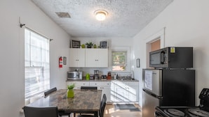 A compact kitchen with white cabinets, a microwave, a stove, and a refrigerator. There is a dining table with chairs and a small plant on the table.