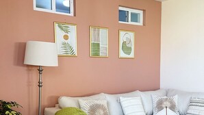 Ein Wohnzimmer mit einer Eckcouch, einer Stehlampe und gerahmten Kunstwerken an der Wand.