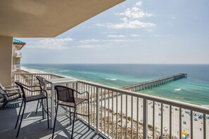 A balcony with two wicker chairs, a view of the ocean, a pier, and a beach with umbrellas. - Absolutely Shore, Navarre Beach (Navarre)