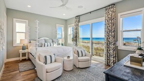 Een slaapkamer met een groot bed, twee fauteuils, een nachtkastje en uitzicht op het strand.