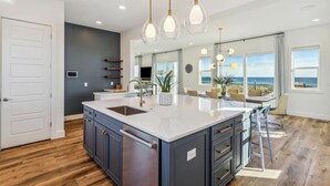 Een moderne keuken met een groot eiland, donkere kastjes en hanglampen.