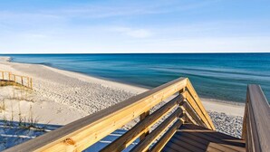 Een houten looppad dat naar een zandstrand leidt, met een helder uitzicht op de oceaan.