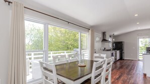 Un coin repas avec une table et des chaises, une cuisine équipée et de grandes fenêtres donnant sur un paysage verdoyant.