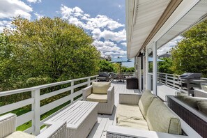 Um deck externo coberto com móveis de vime, churrasqueira e vista para um jardim arborizado.