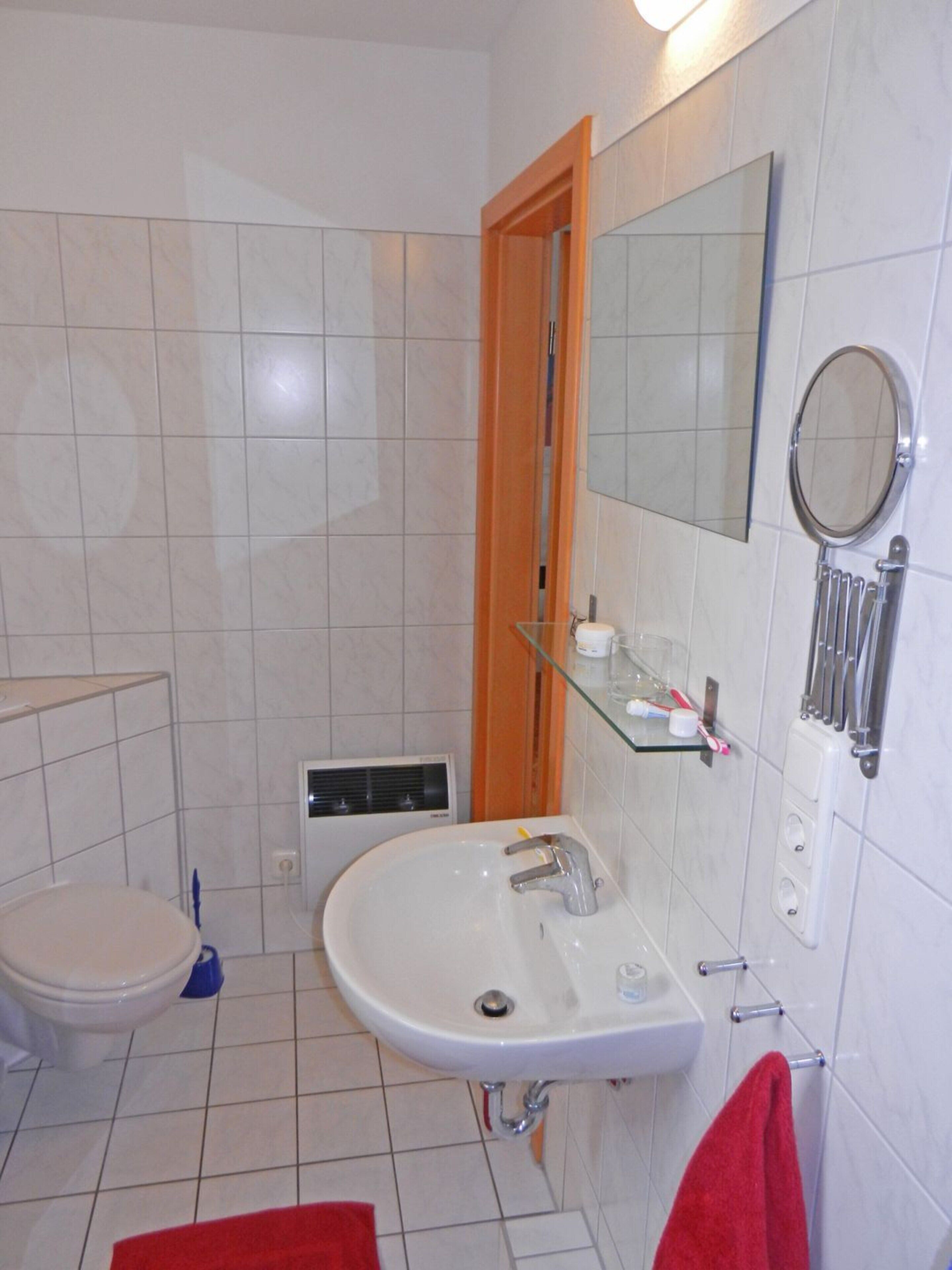 Ein Badezimmer mit weißem Waschbecken, einem Spiegel, einer Toilette und einer Duschkabine.