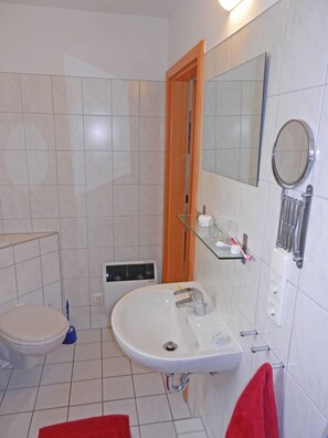 Une salle de bain avec un lavabo blanc, un miroir, des toilettes et un espace douche.