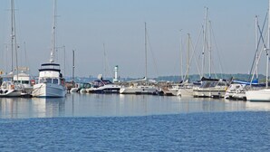 Uma marina com vários barcos atracados, um farol ao fundo e águas calmas.