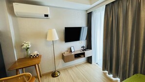 Ein Hotelzimmer mit Flachbildfernseher, Schreibtisch mit Stuhl, Stehlampe, Nachttisch und einem Bett.