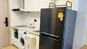 Eine kompakte Küche mit Edelstahlkühlschrank, Waschmaschine, Kaffeemaschine und Spüle.