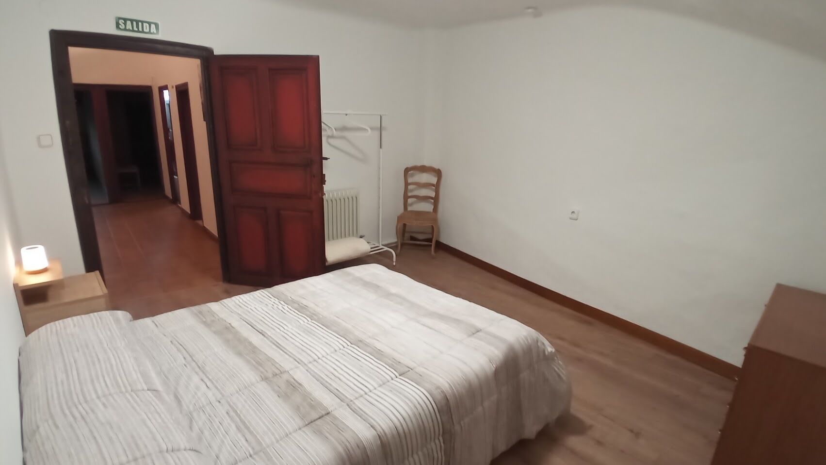 A bedroom with a bed, a wooden door, a radiator, and a chair.