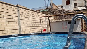 A swimming pool with a ladder, a brick wall, and a small building with a tiled roof in the background. - HOME TO ENJOY IN STYLE !!!! Garden, barbecue, swimming pool, swings, ping-pong. (Arguedas)