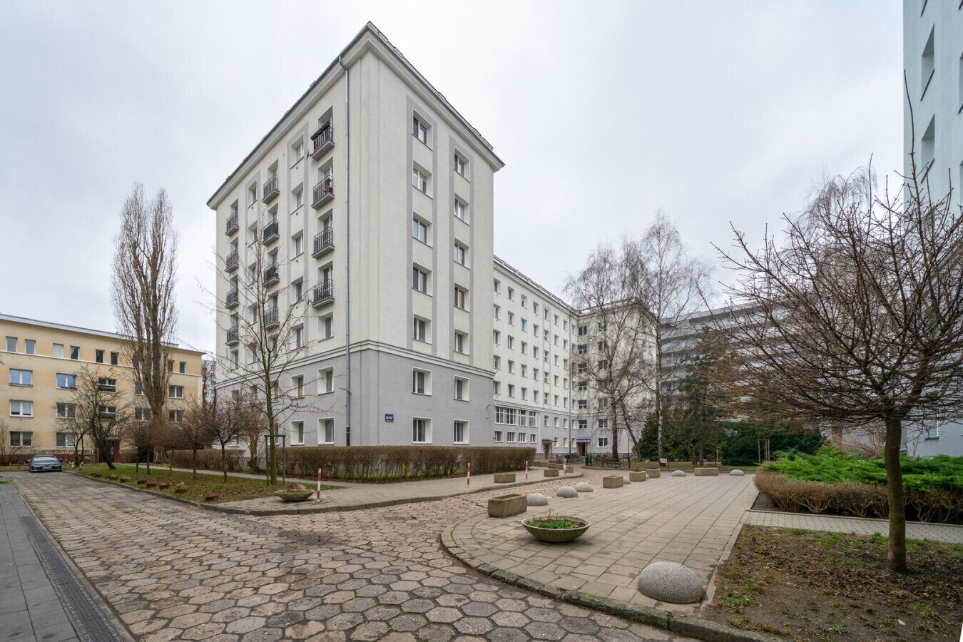 A multi-story residential building with a central courtyard, surrounded by bare trees and a paved walkway.