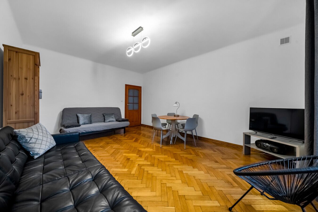 Una sala de estar moderna con un sofá, una mesa de comedor con sillas, un televisor y piso de madera.