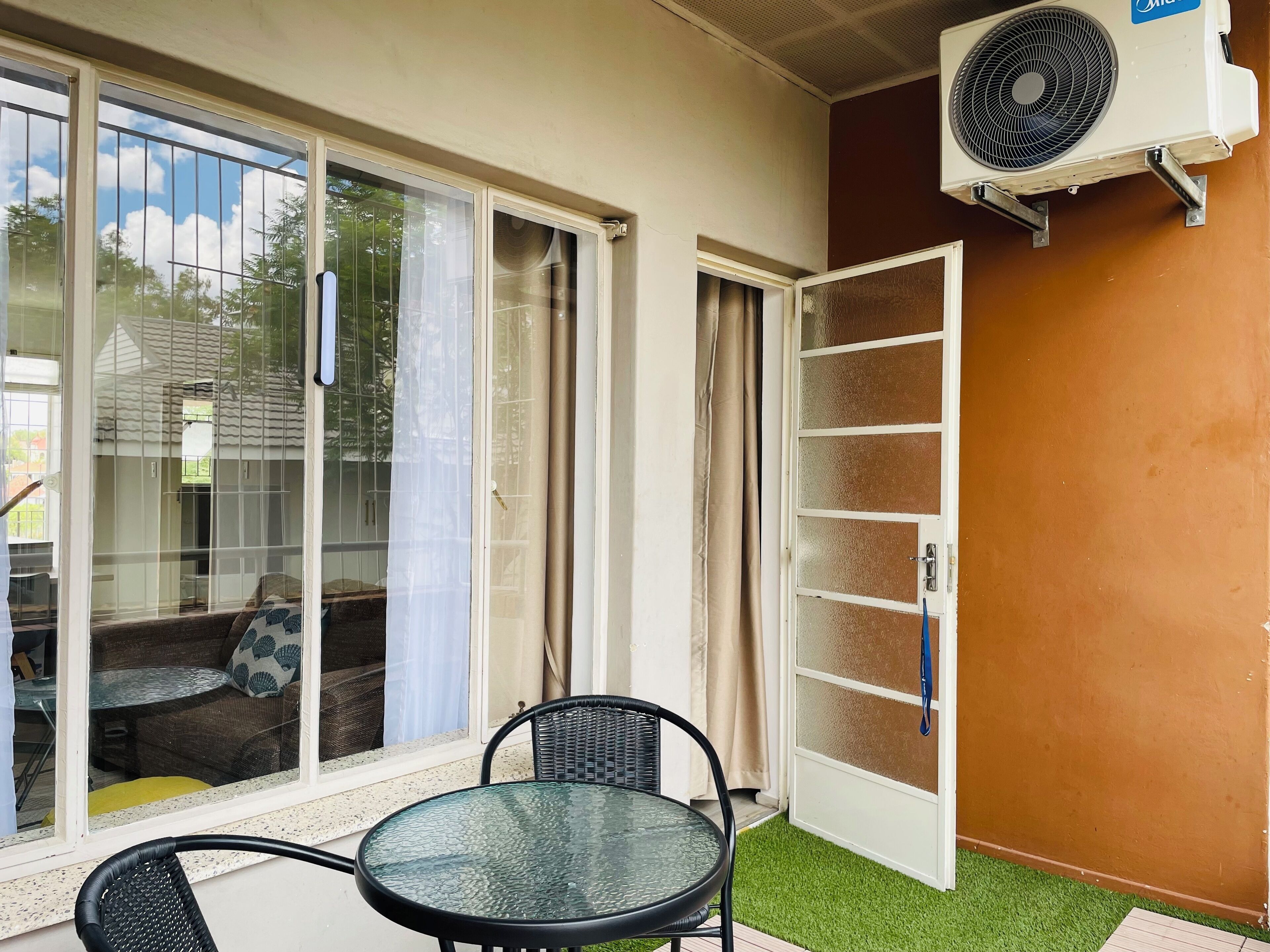 Een glazen deur die leidt naar een balkon met een tafel en stoelen, een airconditioningunit aan de muur en een schuifdeur.