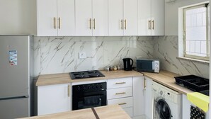 Una cocina moderna con armarios blancos, horno empotrado, microondas y lavadora.