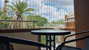 Un balcón con mesa y sillas, vistas a palmeras y un cielo nublado.
