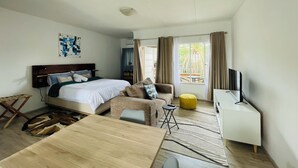 Una habitación de hotel moderna con cama, sofá, una mesita, televisor y ventana con cortinas.