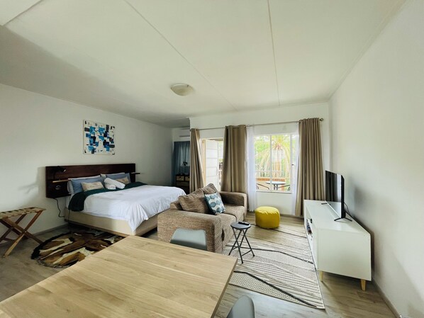A modern hotel room with a bed, a sofa, a small table, a TV, and a window with curtains.