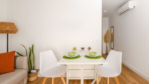 A modern dining area with a white table, two white chairs, and a small plant on the side.