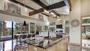 A spacious kitchen with a large island, wooden cabinets, and a black marble countertop. There are multiple windows providing natural light and views of the outdoors. - Breathtaking Views, Indoor/Outdoor Linear Fireplace, Sauna (Angel Fire)