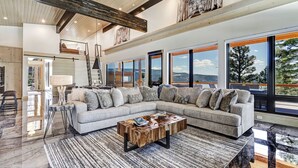 A spacious living room with a large sectional sofa, a coffee table, and large windows offering a mountain view. - Breathtaking Views, Indoor/Outdoor Linear Fireplace, Sauna (Angel Fire)