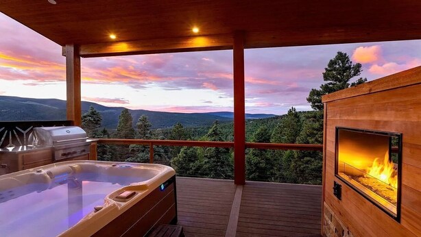 A wooden deck with a hot tub, a grill, and a fireplace. - Breathtaking Views, Indoor/Outdoor Linear Fireplace, Sauna (Angel Fire)