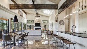 A modern kitchen with a large island, bar stools, and a dining area with a long table and chairs. - Breathtaking Views, Indoor/Outdoor Linear Fireplace, Sauna (Angel Fire)