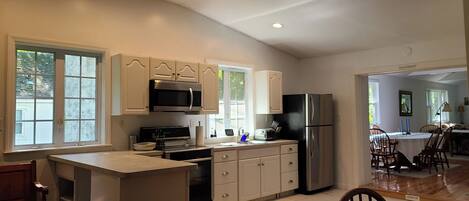 A kitchen with white cabinets, a microwave, a stove, and a refrigerator. There is a window on the left side.