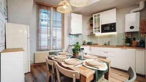 Une cuisine moderne avec des meubles blancs, une table à manger en bois pour six personnes et un four encastré.