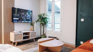 Un salon moderne avec un téléviseur, un meuble en bois, une table basse ronde et deux fauteuils en forme de poire.