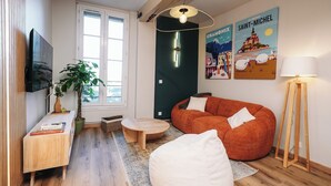 Un salon moderne avec une grande fenêtre, un téléviseur à écran plat, une table ronde en bois, un canapé rouge et un lampadaire.